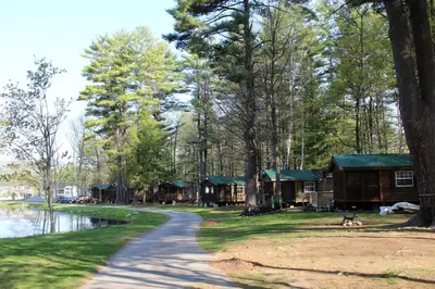 a path leading to cabins in a forest next to a lake at Alpine Lake Lakefront Cabin 5 in South Corinth
