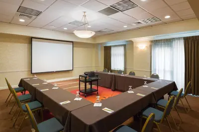 a conference room with tables and chairs and a screen at Hilton Garden Inn Hartford South/Glastonbury in Glastonbury