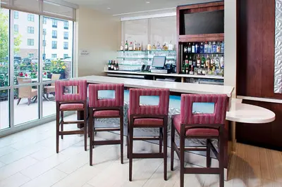 a kitchen with a bar with red chairs and a counter at SpringHill Suites by Marriott Carle Place Garden City in Carle Place