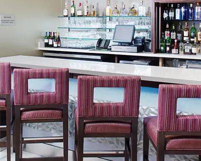 a bar with three chairs and a counter with bottles at SpringHill Suites by Marriott Carle Place Garden City in Carle Place