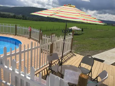 a fence with an umbrella and chairs next to a pool at Apple Inn and Suites Cooperstown Area in Milford