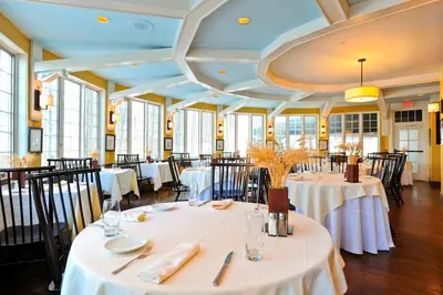 a dining room with white tables and chairs and windows at Avon Old Farms Hotel in Avon