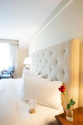 a large white bed with a vase with a flower on a table at The Simsbury Inn in Simsbury