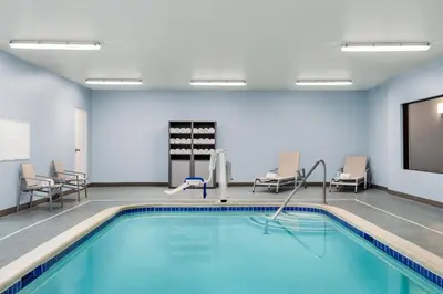 a swimming pool in a room with chairs and a tv at Holiday Inn Express & Suites East Greenbush Albany-Skyline by IHG in Rensselaer