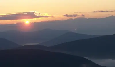 a sunset over a mountain range with the sun setting at Slide Mountain Forest House in Oliverea