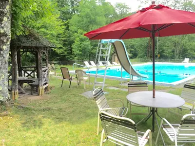 a table with a red umbrella next to a swimming pool at Slide Mountain Forest House in Oliverea