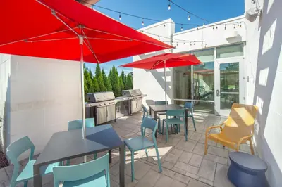 a patio with tables and chairs and red umbrellas at Home2 Suites by Hilton Saratoga Malta in Malta