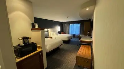 a hotel room with a bedroom with two beds and a desk at Courtyard by Marriott Kingston in Kingston