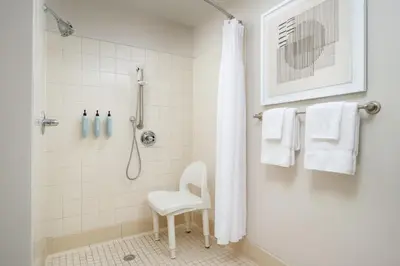 a bathroom with a shower and a white chair at Courtyard by Marriott Kingston in Kingston
