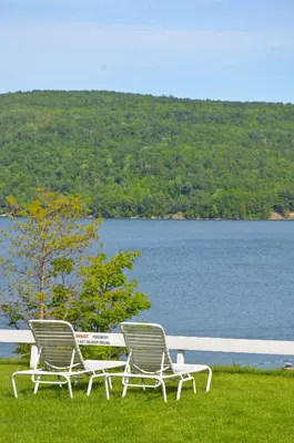 two chairs sitting on the grass near a lake at Lake View Motel in Cooperstown