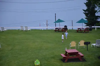 two children walking in a field with picnic tables and chairs at Lake View Motel in Cooperstown