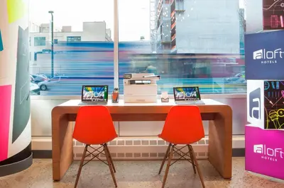 a desk with two red chairs and a laptop on it at Aloft Long Island City-Manhattan View in Queens