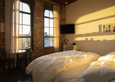 a bedroom with a bed and a table and windows at Wythe Hotel in Brooklyn