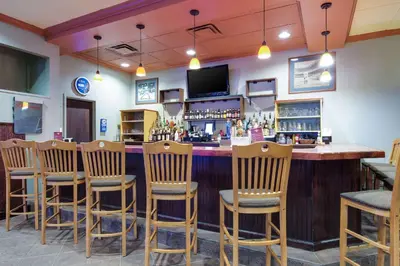 a bar with a row of wooden bar stools at Quality Inn Oneonta Cooperstown Area in Oneonta