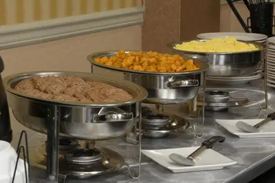 a buffet with three pots of food on a table at Adria Hotel and Conference Center in Queens