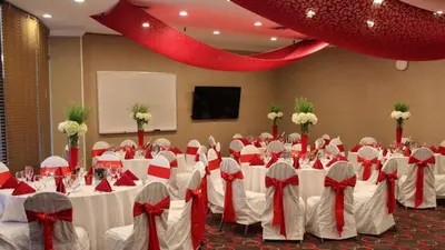 a conference room with white tables and chairs with red bows at Adria Hotel and Conference Center in Queens