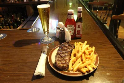a steak and french fries on a table with a glass of beer at Jimmy OConnor's Windham Mtn Inn in Windham