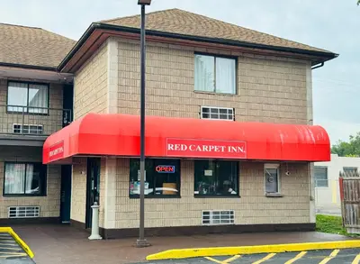 a red canadian inn with a red awning on a building at Red Carpet Inn Norwalk in Norwalk