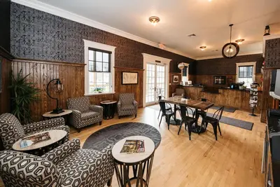 a living room with chairs and tables and a kitchen at The Railroad Inn in Cooperstown