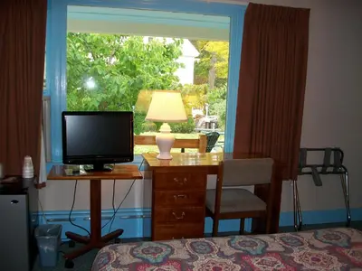 a bedroom with a desk with a television and a window at Mohican Motel in Cooperstown
