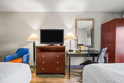 a hotel room with a bedroom with a tv and a desk at Days Inn by Wyndham Utica in Utica