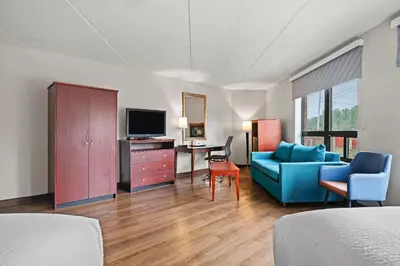 a hotel room with a couch and a desk with a television at Days Inn by Wyndham Utica in Utica