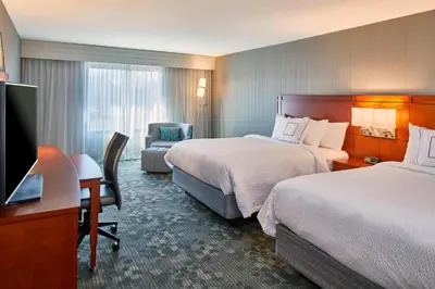 a hotel room with two beds and a desk at Courtyard by Marriott Albany Thruway in Albany