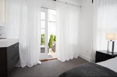 a bedroom with white curtains and a bed and a sink at Station Inn Pawling in Pawling