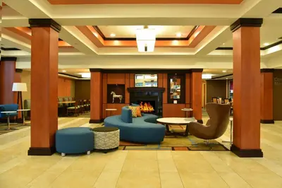 a lobby with a fireplace and blue chairs at Fairfield Inn Hartford Airport in Windsor Locks