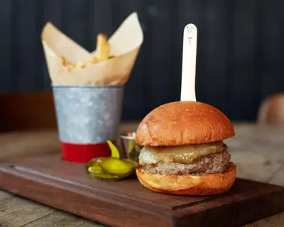 a hamburger on a wooden cutting board with a basket of fries at Wm. Farmer and Sons in Hudson