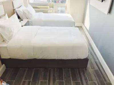 two beds in a hotel room with white sheets at Mayfair Inn and Suites in Queens