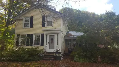 a yellow house with a white door and trees at A Meadow House in Lakeville