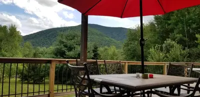 a table and chairs on a deck with a red umbrella at Hunter Mt Amazing Views Catskills! 5 Bedrooms! Best Choice! in Hunter