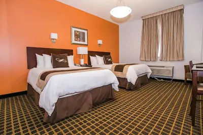 two beds in a hotel room with orange walls at Pointe Plaza Hotel in Brooklyn