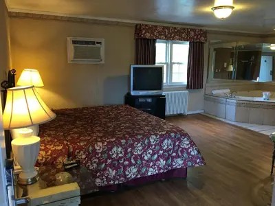a bedroom with a bed and a television and a tub at Colonie Inn and Suites in Latham