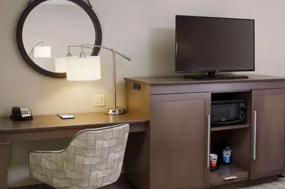 a room with a desk with a television and a mirror at Hampton Inn by Hilton Garden City Long Island in Garden City
