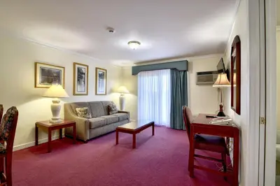 a hotel room with a couch and a desk and a table at Roosevelt Inn & Suites Saratoga Springs in Saratoga Springs