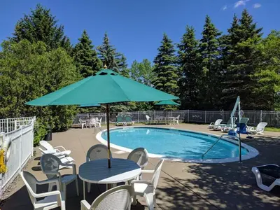 a table with an umbrella next to a swimming pool at The Century House Latham - North Albany, an Ascend Collection Hotel in Latham
