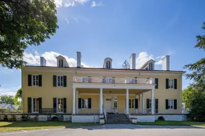 an image of a large yellow house with a balcony at Holiday Inn Poughkeepsie by IHG in Poughkeepsie