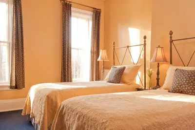 two beds in a bedroom with orange walls and windows at The Inn at Cooperstown in Cooperstown