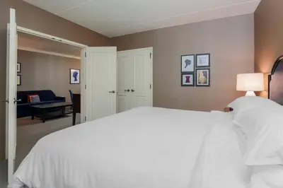 a bedroom with a white bed and a living room at Sheraton Tarrytown Hotel in Tarrytown