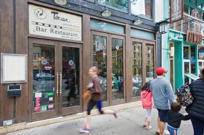 a group of people walking down a sidewalk in front of a bar restaurant at Modern Midtown East Apartments in NYC in New York