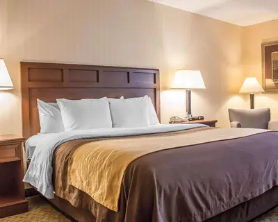 a bedroom with a large bed with two lamps and a chair at Comfort Inn Wethersfield - Hartford in Wethersfield