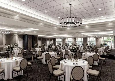 a banquet room with white tables and chairs and a chandelier at The Queensbury Hotel in Glens Falls