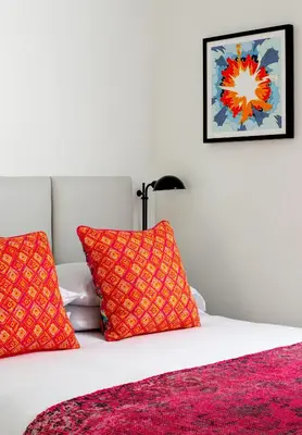 a white bed with two red pillows on it at Bluebird Spa City Motor Lodge in Saratoga Springs