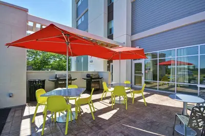 a patio with tables and chairs and red umbrellas at Home2 Suites by Hilton Queensbury Lake George in Queensbury
