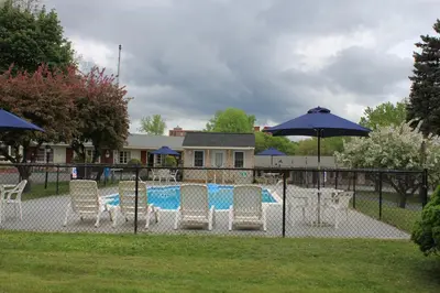 a fence with chairs and a pool and umbrella at Berkshire Inn in Pittsfield