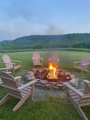 three chairs around a fire pit in a field at August Lodge Cooperstown in Hartwick Seminary