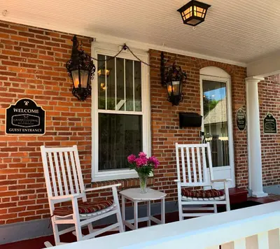three white chairs and a vase of flowers on a porch at Grand Colonial Bed and Breakfast in Herkimer