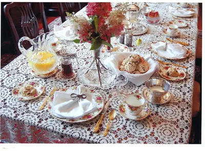 a table with a white lace table cloth with dishes and flowers at Margaretville Mountain Inn B&B in Margaretville